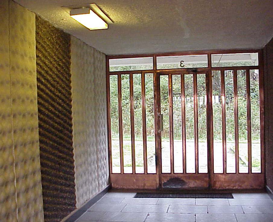 Entréns kopparglans kontrasterar mot väggutsmyckningens mattare betongelement. Notera hur dörrplåten nedtill slitits av alla fotknuffar!