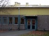 Entré i östra byggnadens östra fasad. Bilden visar fasadens ytterskiva av betong med frilagd ballast (östadssingel) och den panelimiterande fasadplåten, vilka båda kännetecknar de ursprungliga skolbyggnaderna.
