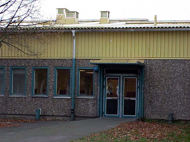 Entré i östra byggnadens östra fasad. Bilden visar fasadens ytterskiva av betong med frilagd ballast (östadssingel) och den panelimiterande fasadplåten, vilka båda kännetecknar de ursprungliga skolbyggnaderna.