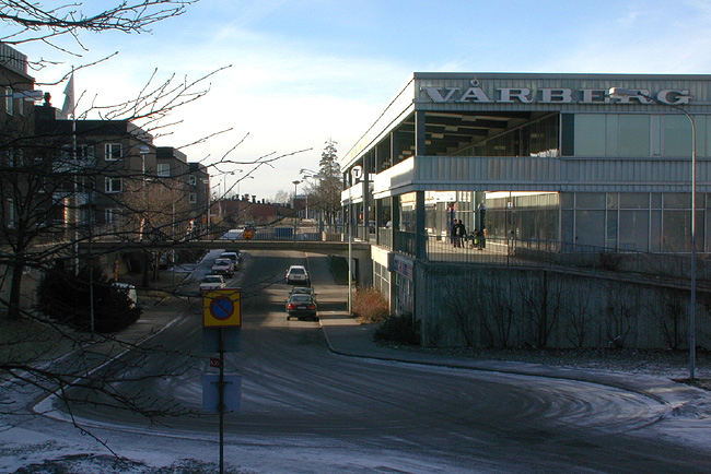 SAK03880 Sthlm, Vårberg, Vårholmen 4 Fjärdholmsgränd 4-38 (jmn nr) Vårbergsplan 3-11(udda nr) från ost


Byggnaden har en arkad mot söder. Den har fasader av brännlackerad korrugerad aluminium som idag är pärlemorskimrande, samt svart och tranperent glas i aluminiumlister.



