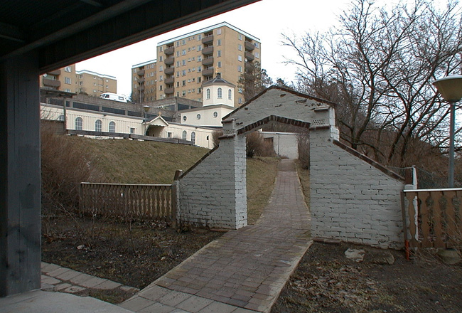 Porttal i slammat tegel vid entrén från centrum. 

SAK03829 Sthlm, Vårberg, Vårholmen 2, Fjärdholmsgränd 48 från sydväst