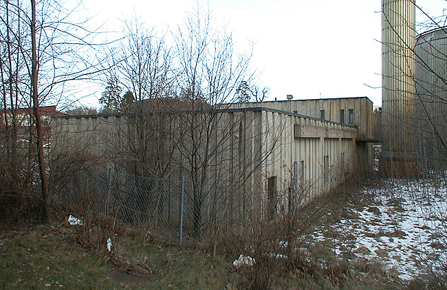 SAK03535 Sthlm, Vårberg, Kummelholmen 2, Vårholmsbackarna 120, från sydväst. Byggnadens västra gavel och södra långsida. Den höga skorstenen ligger bara någon meter från byggnaden. 







