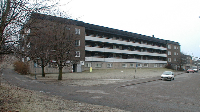 SAK03694 Sthlm, Vårberg, Jungfruholmen 2, Vårbergsplan 14-60 (jmn nr) från nordost.

Det östligaste husets norra fasad, med loftgångar och hög suterrängvåning.
Till höger matargatans vändplats.