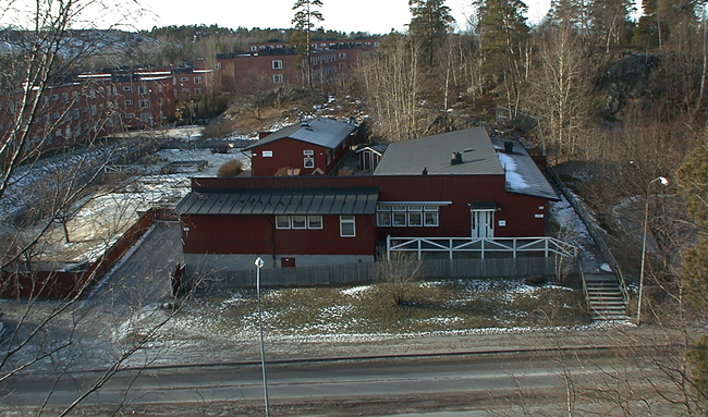 Vy från O. Notera den vinkelbyggda längans speciella takform. I bakgrunden HSB:s lamellhus i kv. Kummelholmen m.m. 

SAK03508 Sthlm, Vårberg, Byholmen 3, Vårholmsbackarna 114, från ost