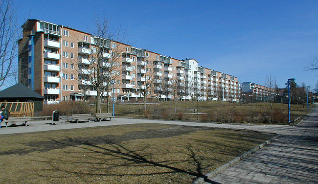 SAK05212 Sthlm, Rinkeby, Kvarnhuset 1, Stavbygränd 1-19 (udda nr) från sydväst

Huset ligger som en bullerskyddande mur ut mot Hjulstavägen i norr. Framför sydsidan bildas en stor öppen gårdsyta. Här låg tidigare ett par lamellhus. Husets mittparti markeras genom att fasaden putsats och försetts med en frontespis.





