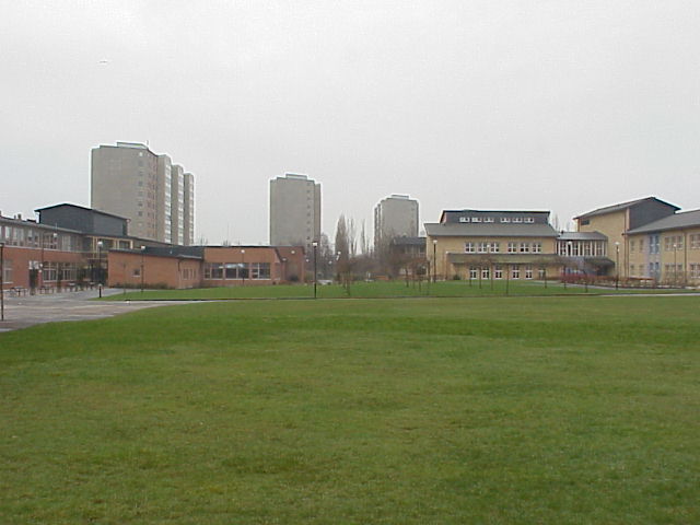 Skolgården sedd från norr. Till vänster ligger den större skolsalsbyggnaden och till höger den sentida vinkelbyggnaden med fasader av gult tegel.