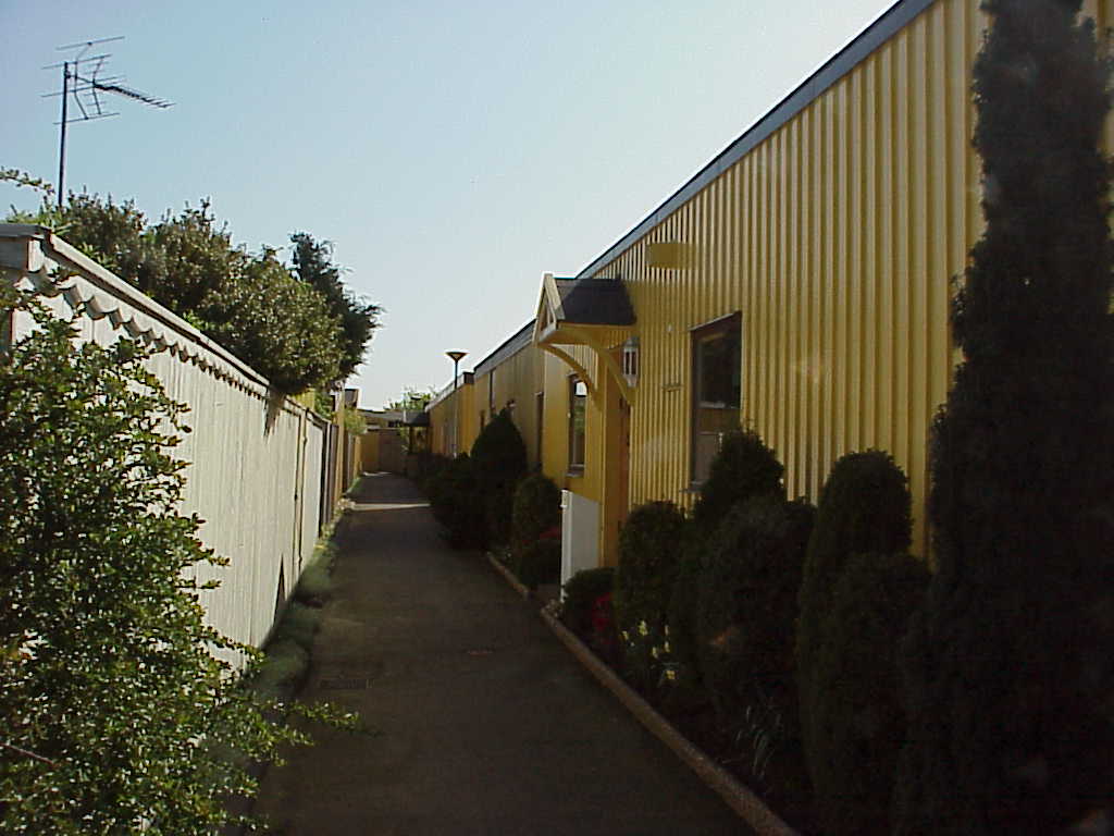 Gångstråken kantas av slutna platta fasader och höga staket som omger atriumhusens trädgårdar. Regntaket över entrén är ett sentida tillägg som förekommer relativt ofta i området.