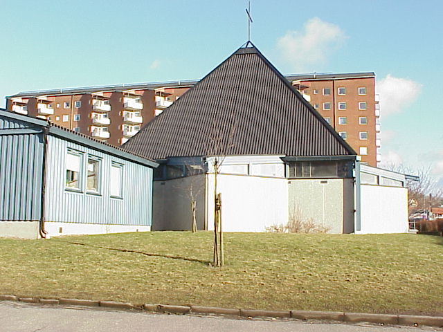 Del av kyrkans västfasad. Det i plan stjärnformade kyrkorummet i förgrunden och skivhuset vid Brunnsbo torg i bakgrunden.