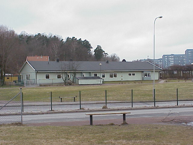 Daghemmets ena byggnadskropp är placerad längs med den större Litteraturgatan. Till höger om daghemmet ligger Brudbergsskolans två byggnader och bakom dessa Blå stadens höghus.