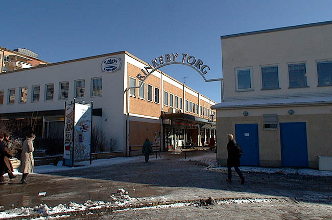 Rinkeby, Kvarnberget 8, Rinkebytorget 1.

Över gågatan in till torget från väster finns denna ljusskylt. På sin västra gavel har huset i Kvarnberget 4 ett utskjutande parti med lastkaj. Mellan lastområdet och gågatan in till torget finns en formgjuten betongmur med låga planteringslådor.



 

 