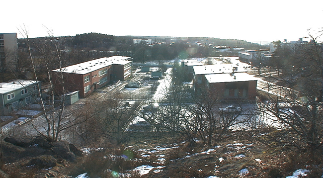 Översiktsbild av skola som byggts om och förtätats till bostadsområde. Till vänster i bilden nybyggda radhus, till höger parkeringsdäck. 

SAK03516 Sthlm, Vårberg, Aspholmen 1, Vårholmsbackarna 83-125 (udda nr) från norr
