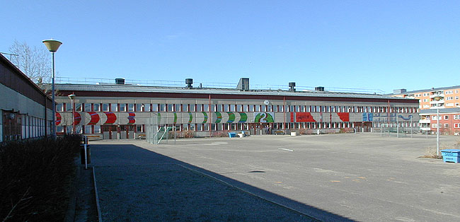 SAK07056 Sthlm, Hjulsta, Harlinge 1, Hjulsta backar 4,6, från sydost

Gymnastikbyggnaden, huvudbyggnaden och skolgården. Huvudbyggnadens fasad är dekorerad med emaljerade plåtar i olika mönster och kulörer, signerade L Strunke.
