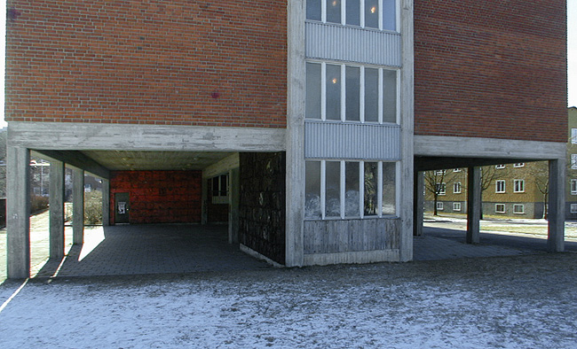 Vid norra änden av huset är bottenvåningen "utskuren" och ersatt av kraftiga betongpelare. Ett trapphus, placerat i gavelns mittaxel, utgör ett undantag.
SAK03901 Sthlm, Vårberg, Byholmen 1, Vårholmsbackarna 100, från norr











