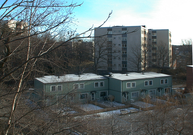 Den östra radhuslängans trädgårdssida. 
SAK03509 Sthlm, Vårberg, Aspholmen 1, Vårholmsbackarna 83-125 (udda nr) från nordväst
