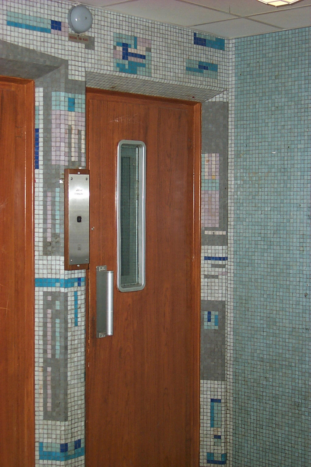 Trapphuset med mosaik på väggarna och ådringsmålade hissdörrar.