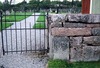 Askums gamla kyrkogård. I kyrkogårdsmuren finns sten från den rivna kyrkan, som den smala refflade stenen näst överst i grindstolpen.