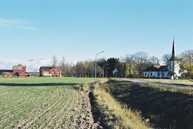 Kyrkomiljön från väster. Till vänster i bild det tidigare prästgårdsjordbruket. Prästgårdens mangårdsbyggnad med flygelbyggnader är skymd av de stora träden i trädgården (mellan kyrkan och gården).