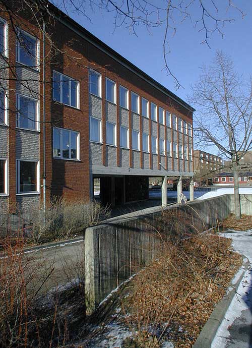 Vårberg, Byholmen 1, Vårholmsbackarna 100, från sydost. Vårbergsskolans "pelarhall" passeras dagligen av de boende i lamellhusområdena på väg till centrum.
