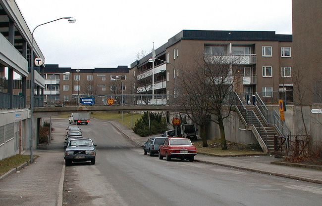 Sthlm, Vårberg, Jungfruholmen 2, Vårbergsplan 14-60 (jmn nr) från väst 

En gångbro leder in till centrum från söder.
