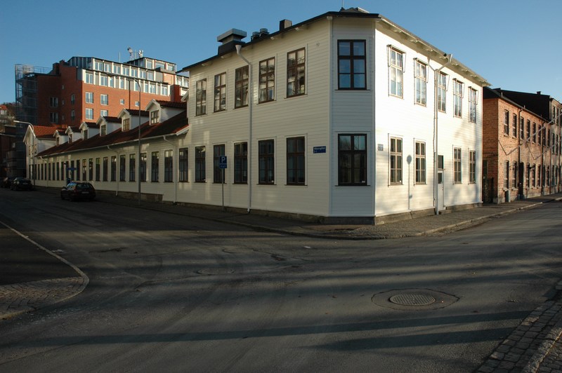 Hästskosömfabriken, närmast träbyggnaden i korsningen Åvägen-Vädursgatan. Envåningsdelen fungerade som hästskosömfabrikens maskinsal medan tvåvåningsdelarna fungerade som kontor och lager. Till höger tegelbyggnaden, ursprungligen en sågsmedja, efter 1919 fabriksbyggnad för tillverkning av tvål och kosmetika.