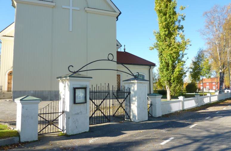 Grindstolparna av putsad betong med svarta smidesstaket från 1930-talet ger en fin och passande inramning till kyrkan. De har ett högt miljöskapande värde. Här syns östra entrén, med koret och sakristian i bakgrunden. Den röda byggnaden som skymtar till höger i bild är gamla kyrkoherdebostaden (numera pastorsexpedition).