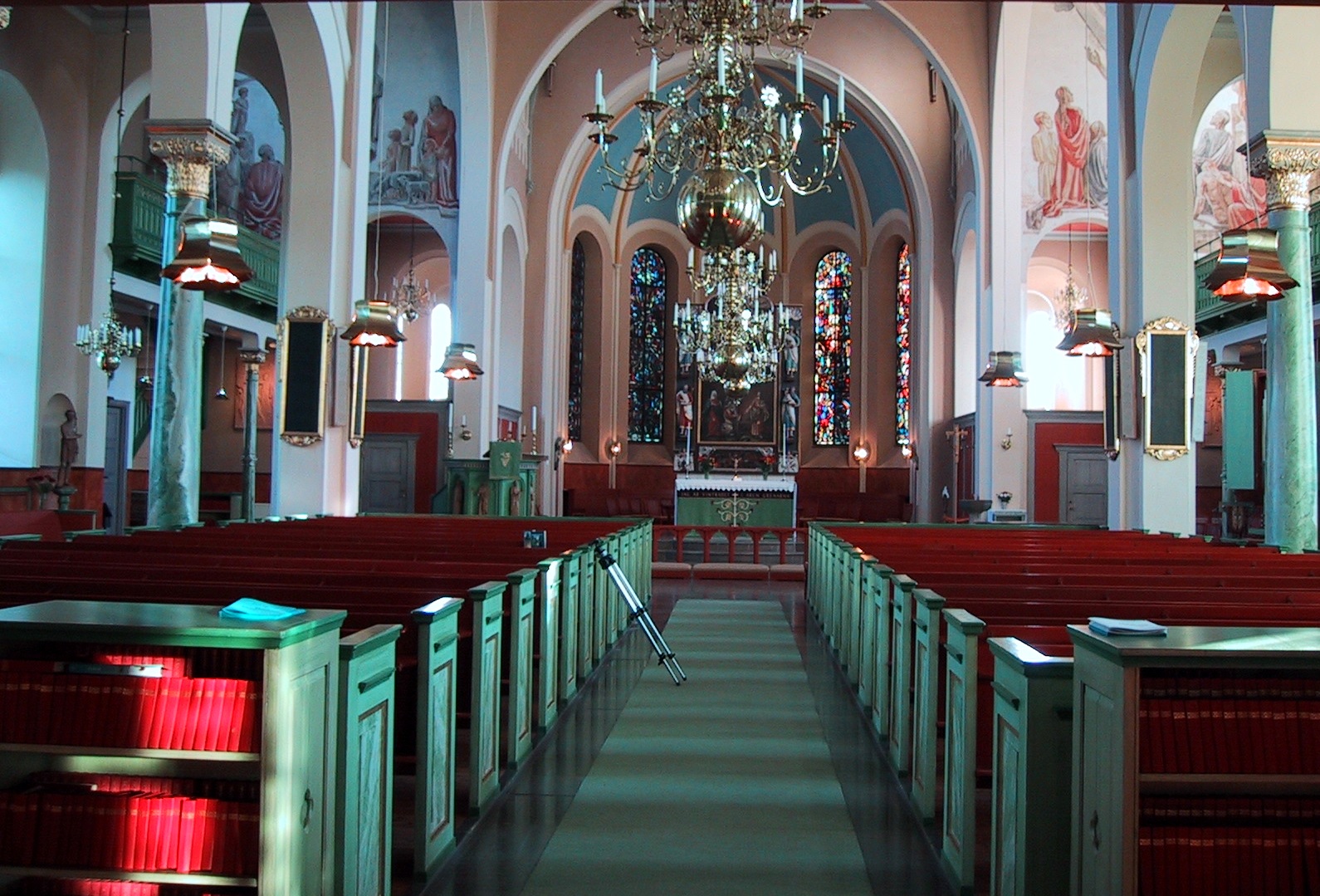 Nora kyrka, interiör, kyrkorummet. 
Det treskeppiga kyrkorummet är utformat som en basilika med plana innertak, högre i mittskeppet och lägre i sidoskeppen, uppburna av gjutjärnskolonner.

