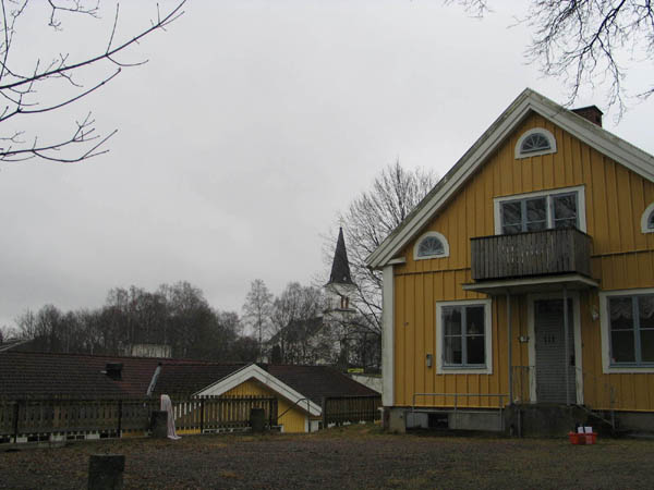 Kyrka och kyrkogård från präsgården (gula byggnaden) i nordväst.