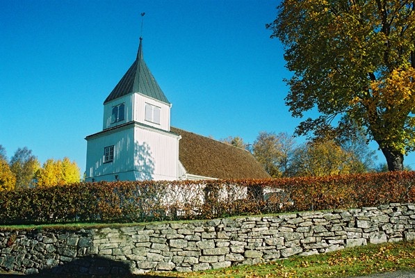 Grönahögs kyrka med stödmur och häck sedd från sydväst.