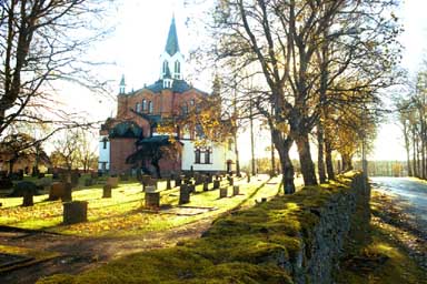 Tranemo kyrka med västra kyrkogårdsmuren utmed tillfartsvägen, från NV.
