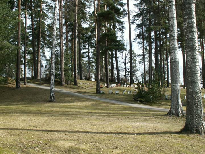 Skogskyrkogården med de höga träden bland gravvårdarna i den kuperade terrängen