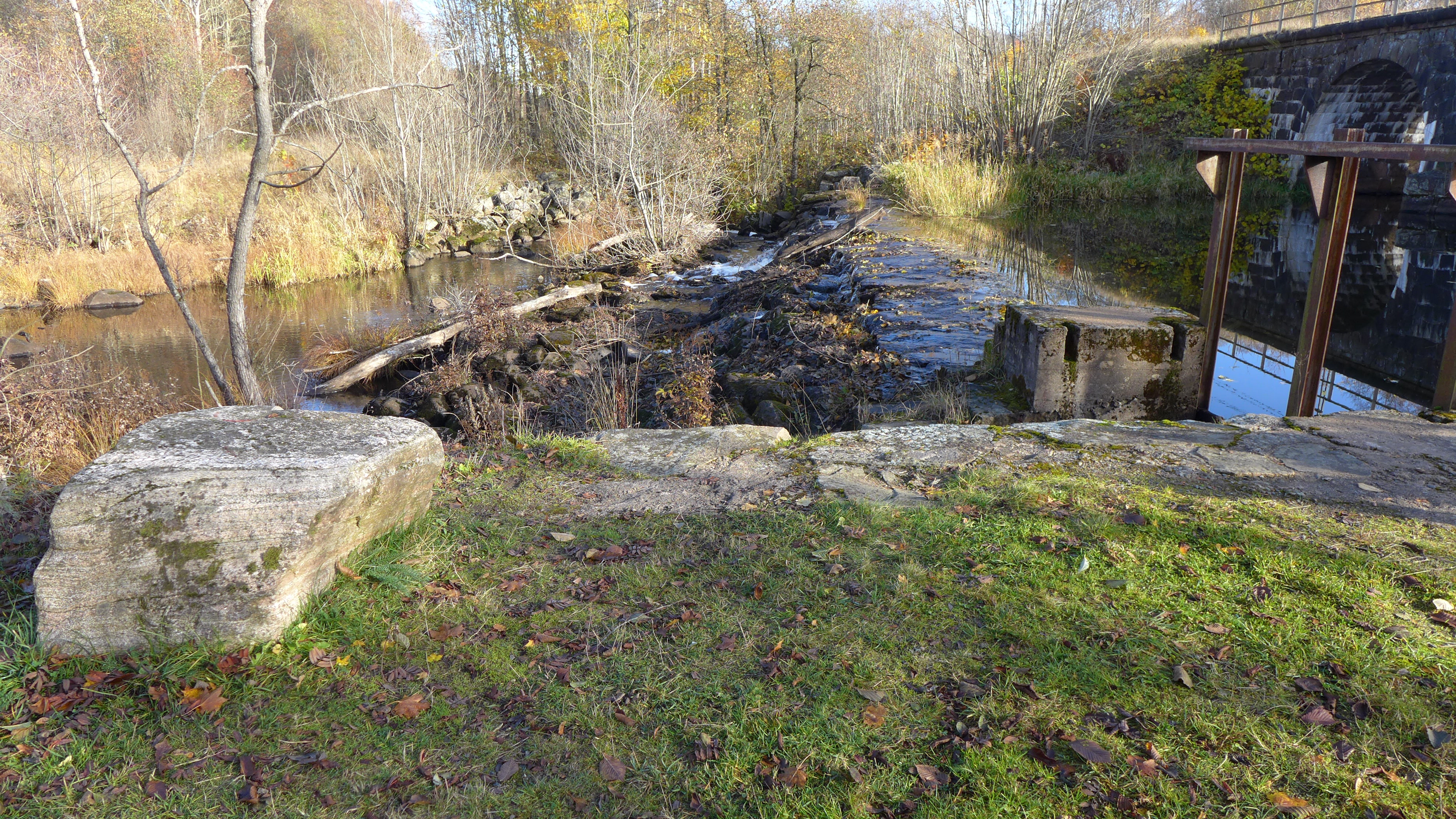 Överfallsdammen består av en gjuten tröskel på natursten. Här finns också en utskovslucka för ytterligare avbördning av dammen.