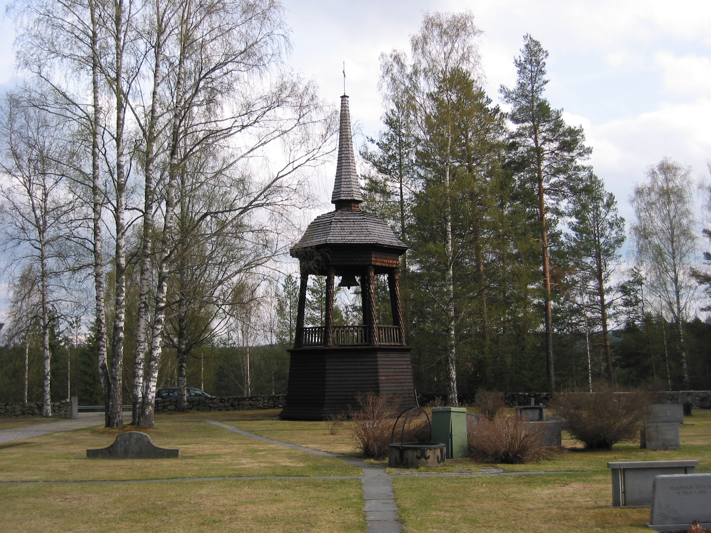 Alby gravkapell/kyrkas kyrkogård, klockstapeln, vy från norr. 

I söder står en klockstapel i trä strax väster om den grusade raka gången fram till kyrkan. Den åttkantiga klockstapeln, ritad av arkitekt Per Österlund från Sundsvall 1931, är en hembygdsinspirerad pastisch med träpanel på förvandring i rådstugan, kyrkspånklädda stolpar med papyruskapitäl i den öppna övre våningen samt barocksvängt tak med uppskjutande spira, allt klätt med rundspån. Helt tjärad
