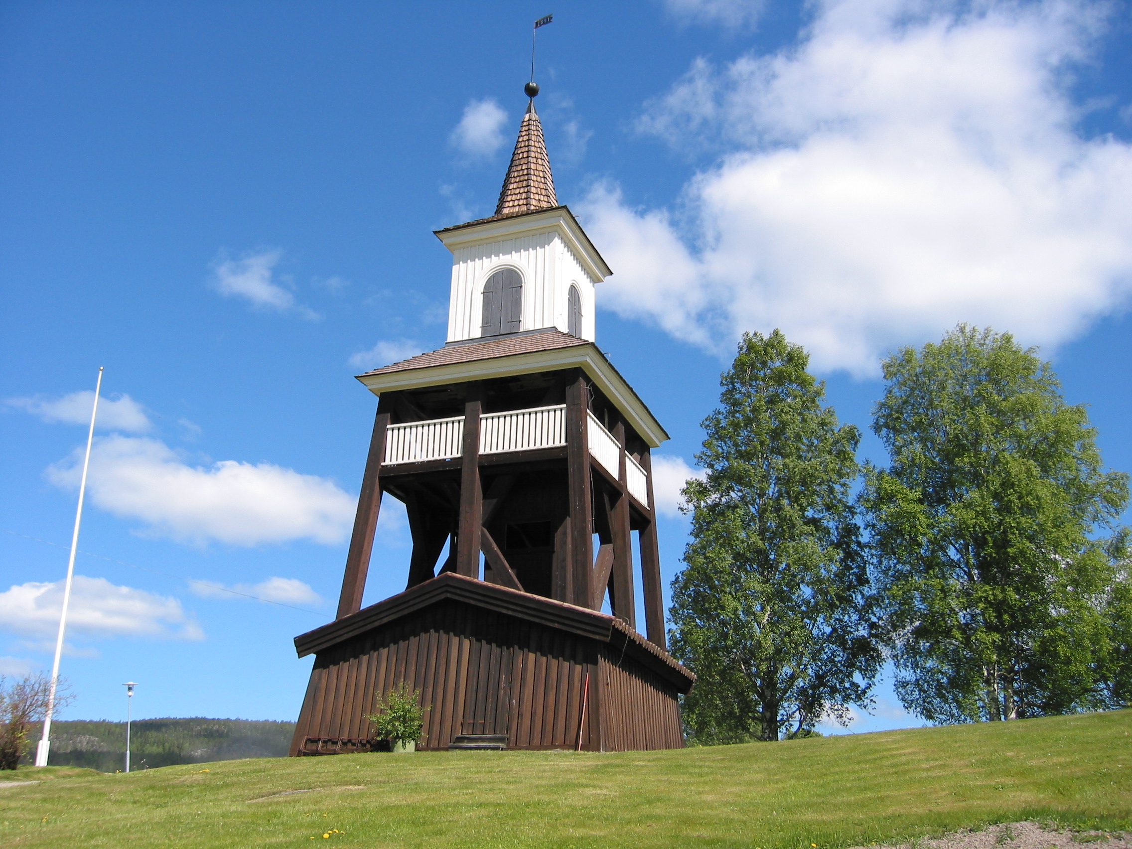 Överlännäs kyrkas kyrkogård. Klockstapeln, vy från sydöst.

Utanför kyrkotomten i väster, men öster om grusvägen, står en klockstapel med åtta fyrkant-stolpar, som fått sin nuvarande form 1891 och ombyggd 1951. Fyrkantig grundplan med totalt åtta inåtlutande fyrkantstolpar i hörnen och en mitt på varje sida. Krysstag i varje sida. En central rund mittstolpe stödjer klockupphängningen med tre åsar, de yttre med fyrkantsned-strävor. Brunmålad locklistpanel i rådstugan, brunt sadeltak med halvrund omlottlagd ved, öppen klockvåning med vitmålat träräcke, spånklätt tälttak ur vilket lanterninen skjuter upp med vitmålad stående locklistpanel och dubbla, svartmålade rundbågade träluckor i alla väderstreck, spånklädd spira  med krönande klot i svart plåt samt årtalsvimpel.