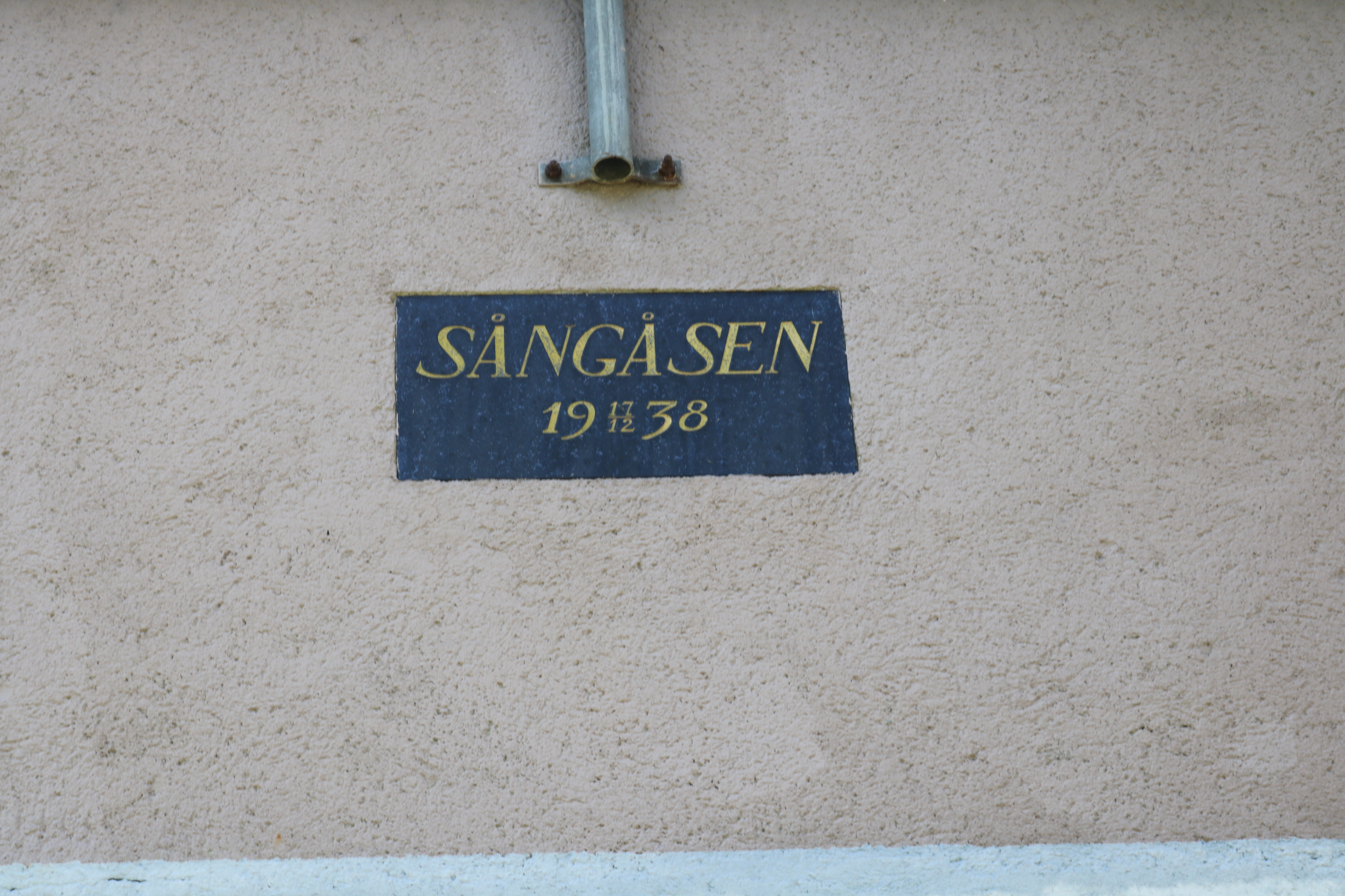 Plakett på fasaden över dörren på kraftveket. "SÅNGÅSEN 1938" i guldfärg. 