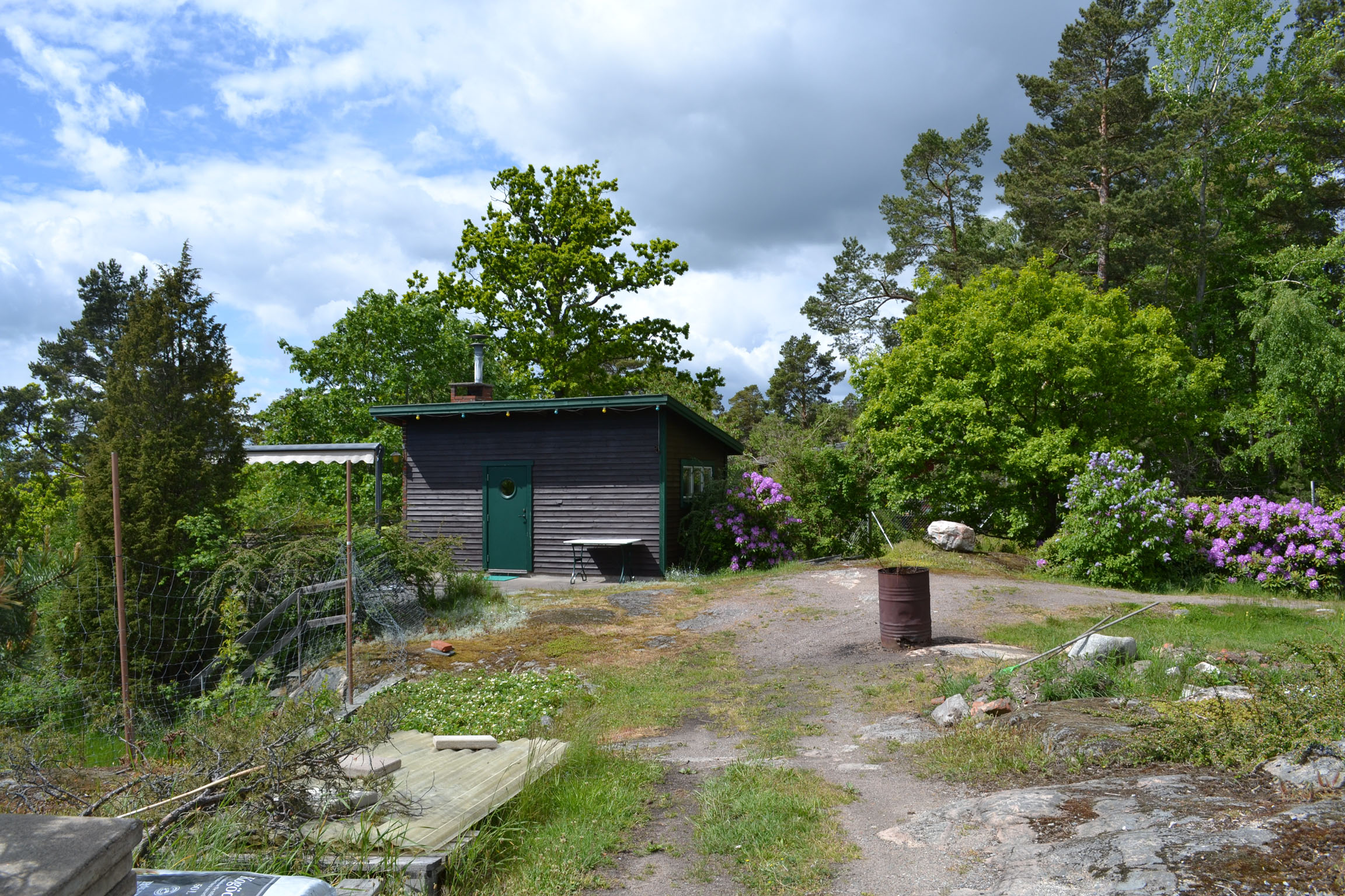 Stugan med omgivande trädgård sedd från Bryggvägen.