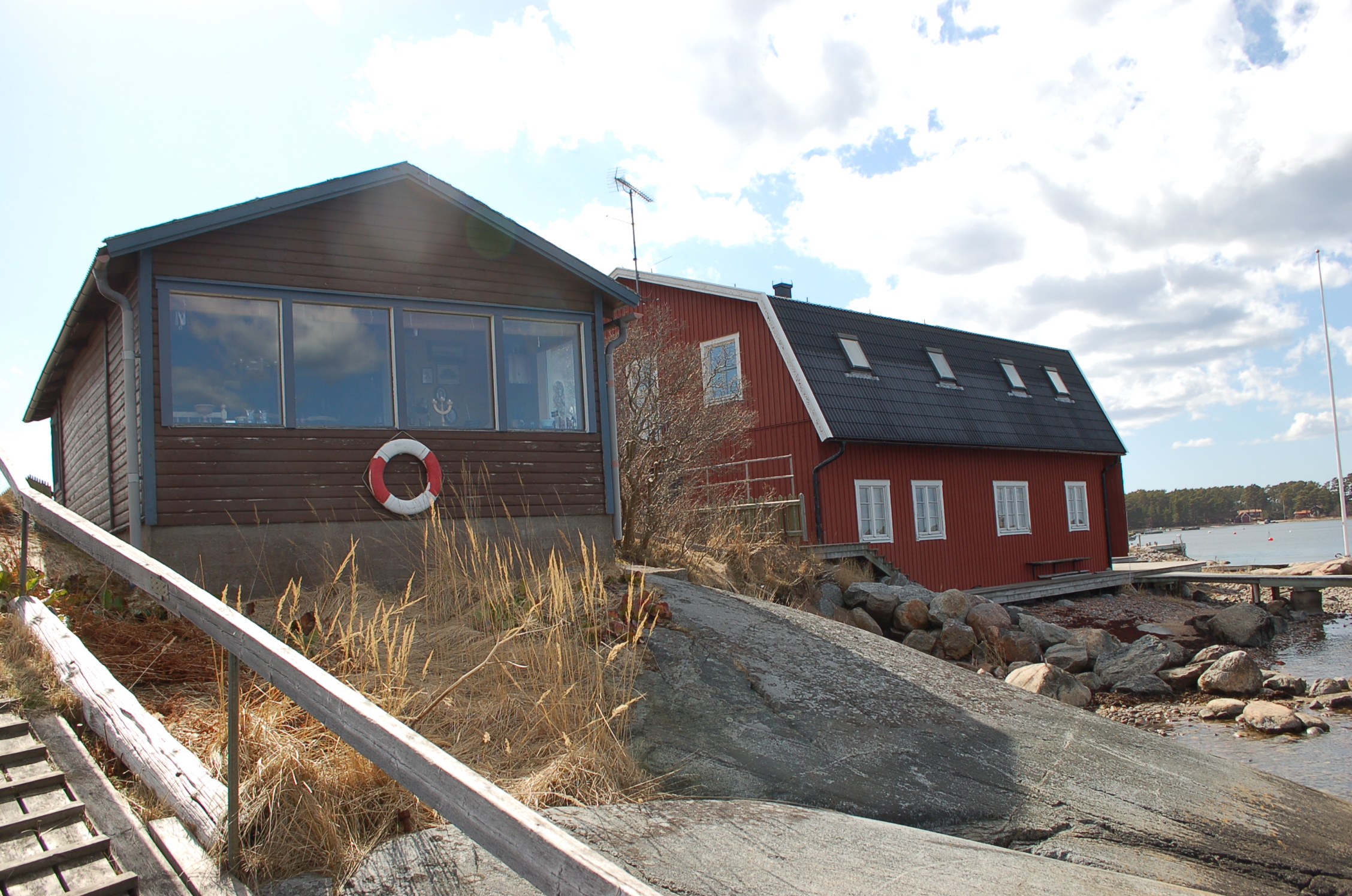 Stugan samt en av byggnaderna tillhörande Sandhamns varv i bakgrunden.