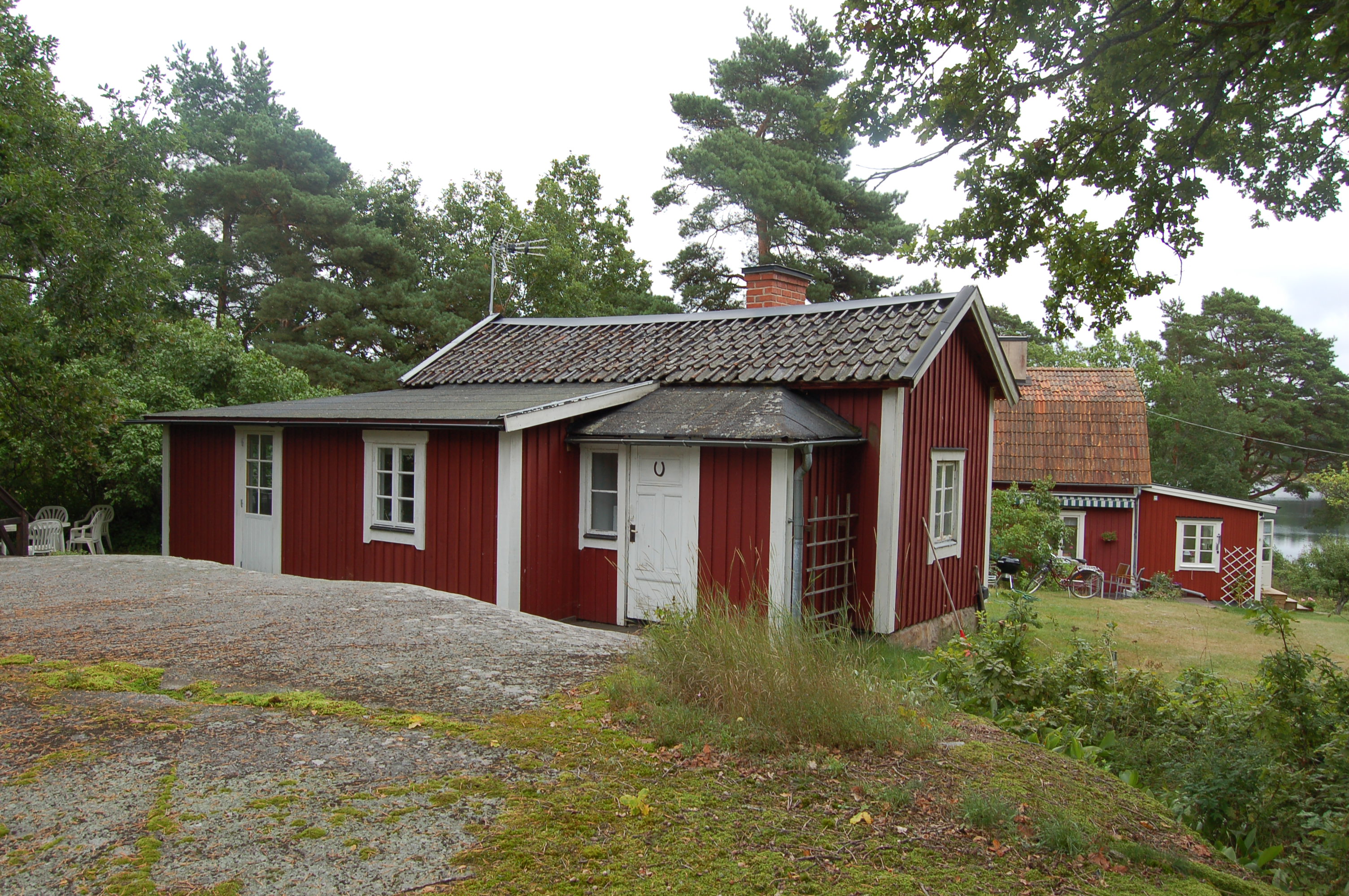 Tillbyggd stuga med omgivande trädgård.