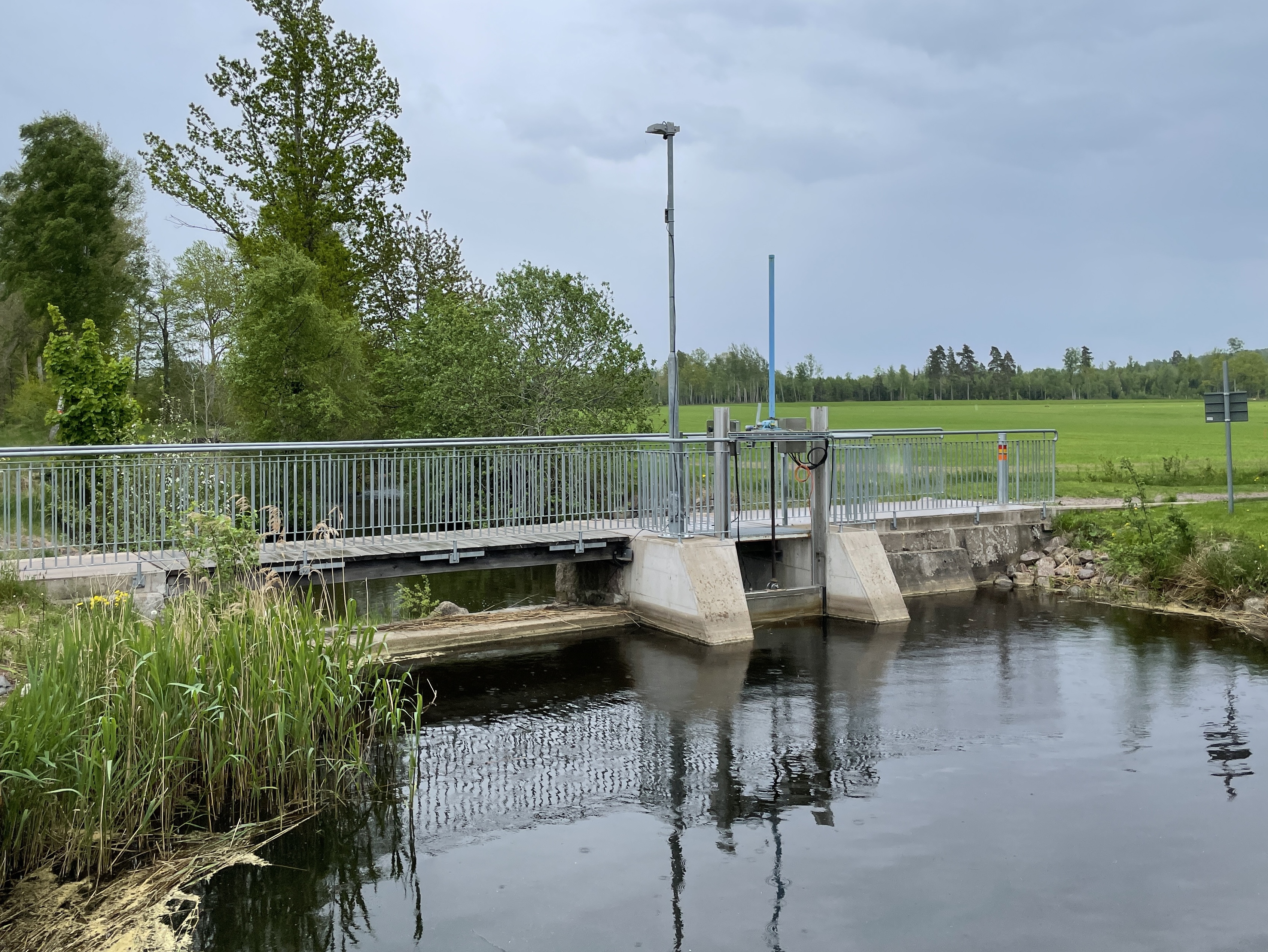 Dammen sedd  från sjösidan.  Till vänster, utanför bild, har en fisktrappa anlagts med ett 
tillhörande omlöp som passerar under gång- och cykelvägen genom en betongtrumma. 