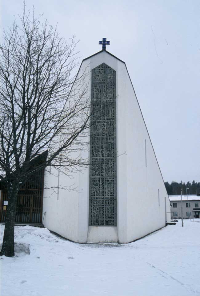 Åmotsfors kyrka, exteriör. 

I det nordöstra hörnet reser sig taket kraftigt och här finns i muren ett ljusinsläpp försett med glasmosaik av Ralph Bergholtz och Randi Fisher.

Fotograf: Lena Magnusson