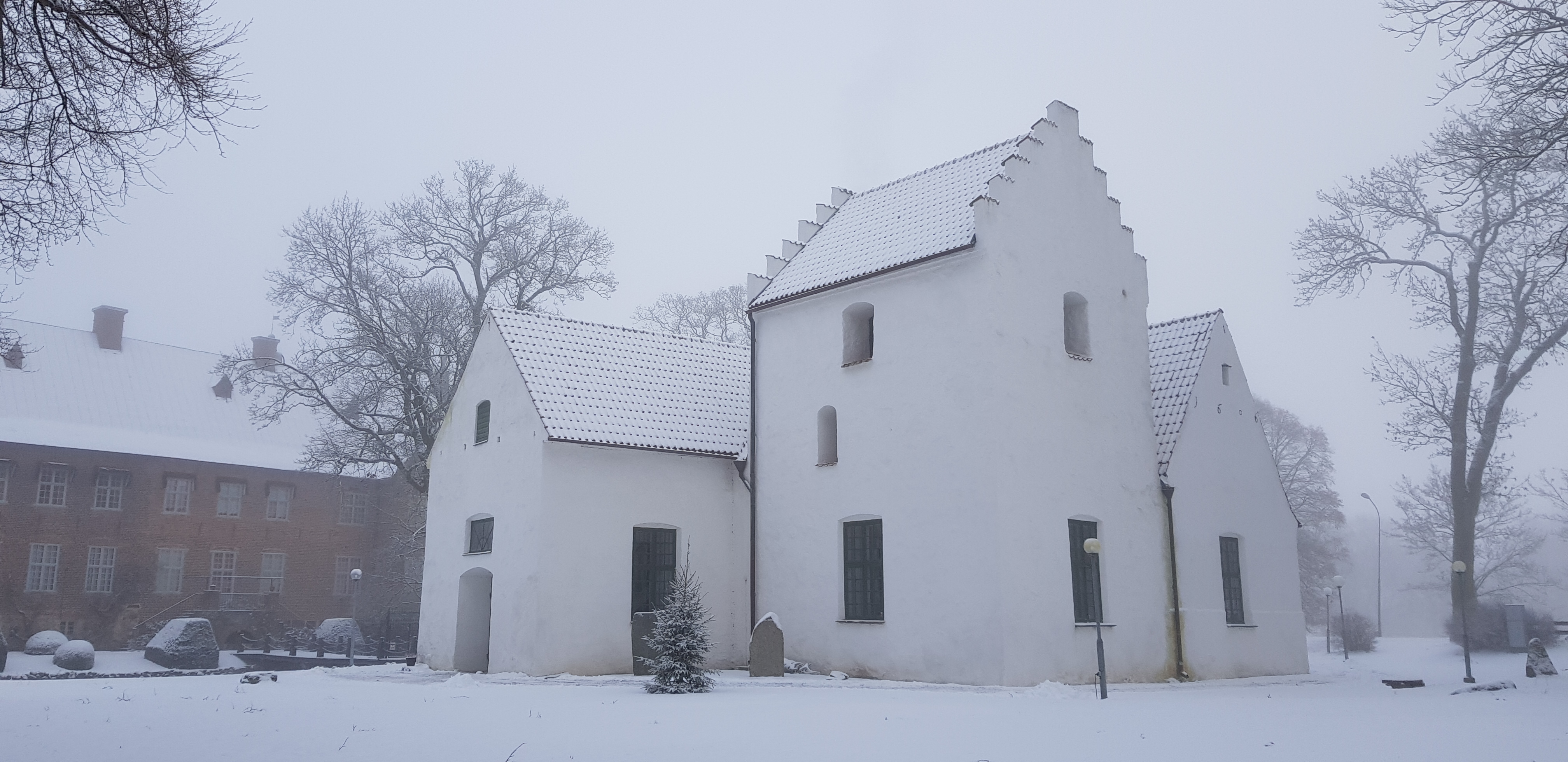 Trolle Ljungby kyrka med entré i väster och klocktorn samt tillbyggnad från 1606 i söder. I fonden, i norr, syns Trolle Ljungby slott. 