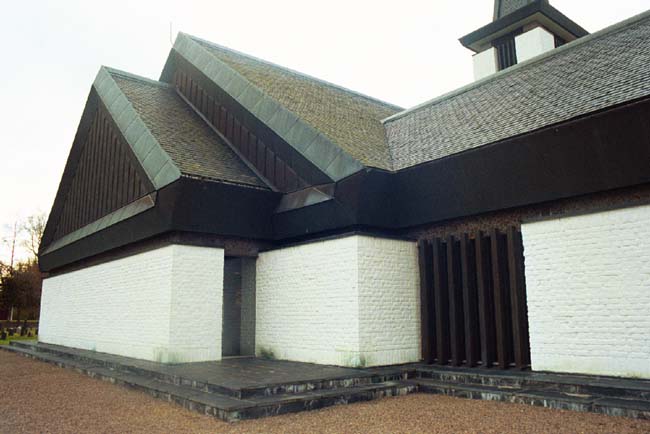 Dalstorps kyrka med koret och del av sakristian sedd från nordöst. Runt kyrkan löper en skiffersockel i två avsatser. Det skifferklädda sadeltaket har detaljer i kopparplåt.