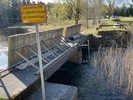 Dammen har två öppningar som är försedda med ett slags vippluckor. Till höger syns det 
ena av två bevarade murade brofästen och spår efter tidigare vägräcken.