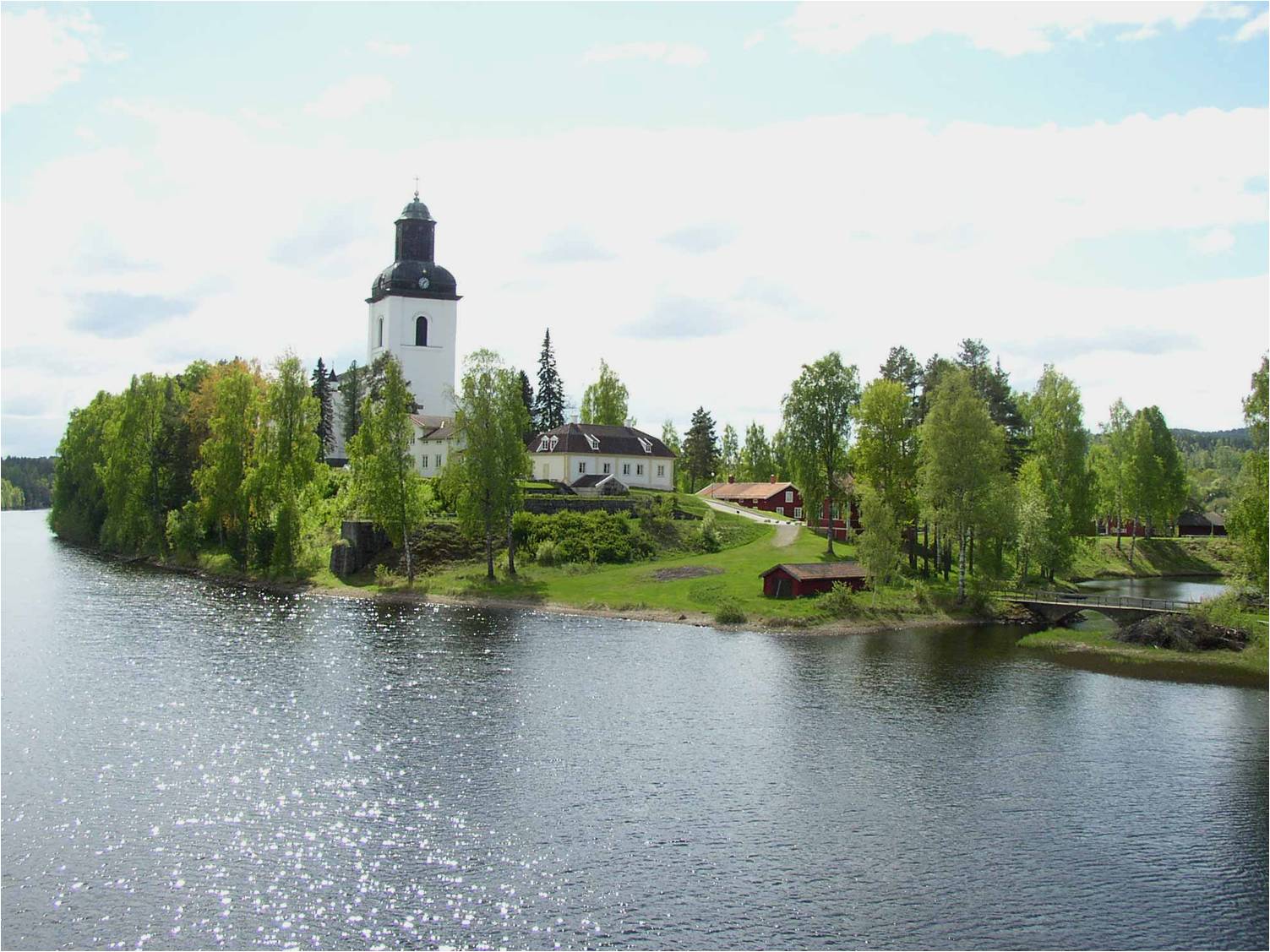 Kyrkön i Järvsö med kyrkan samt prästgården från bron över Ljusnan i nordost. 