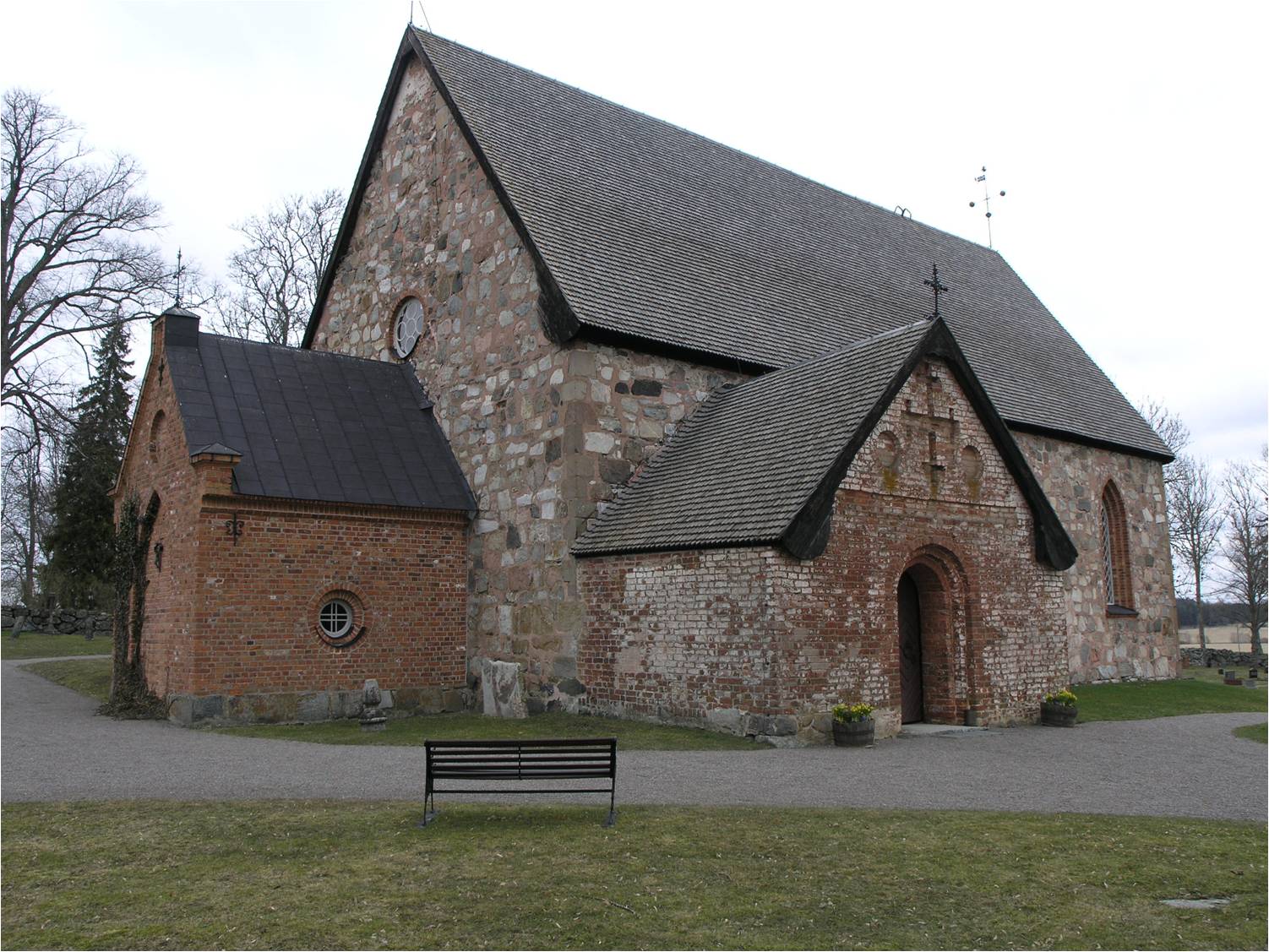 Håtuna kyrka från sydväst med det södra vapenhuset från 1400-talets mitt med rundbågig portal och blinderingar samt det västra vapenhuset från 1870-tal.