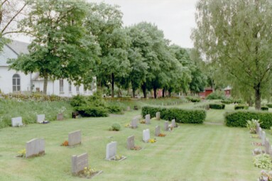 Fristads Nedre kyrkogård på nordvästra sidan och arrendatorsgårdens byggnader skymtande i fonden.